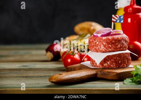 Homemade hamburgers. Raw beef patties and ciabatta bread with other ingredients for hamburgers on wooden background Stock Photo