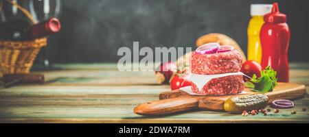 Homemade hamburgers. Raw beef patties and ciabatta bread with other ingredients for hamburgers on wooden background Stock Photo