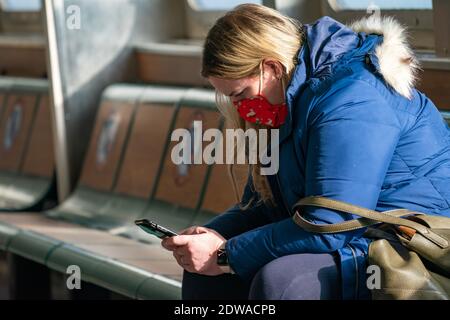 New York, United States. 22nd Dec, 2020. A woman wearing a face mask uses a smartphone at the Staten Island Ferry.Many holiday events have been cancelled or adjusted with additional safety measures due to the ongoing coronavirus (COVID-19) pandemic. Credit: SOPA Images Limited/Alamy Live News Stock Photo