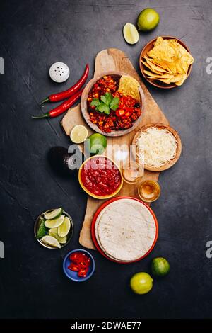 Concept of Mexican food (corn tortillas, nachos, salsa, avocado, limes, cheese, chili con carne) flat lay Stock Photo