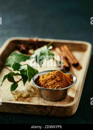 Indian or pakistani masala powder and spices on wooden tray. Small metall bowl with dry curry garam masala mix spices blend, green bay leaf, cinnamon Stock Photo