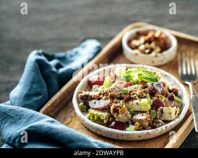 Waldorf salad on wooden tray. American fruit and nut salad with apples, celery, grapes, chicken meat, dressed mayonnaise. Craft plate with ready-to-ea Stock Photo