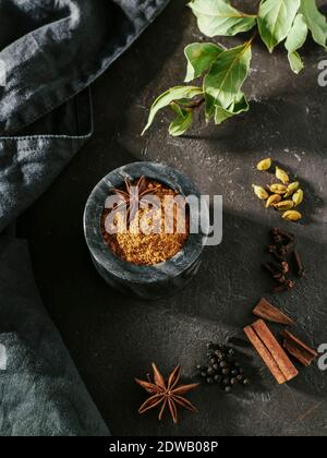 Indian or pakistani masala powder and spices on black backround. Small black marble bowl with dry curry garam masala mix spices blend, green bay leaf, Stock Photo