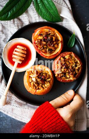 Apples stuffed with walnuts and drizzled with beetroot syrup on a black plate, a woman wearing red sweater holding it. Stock Photo