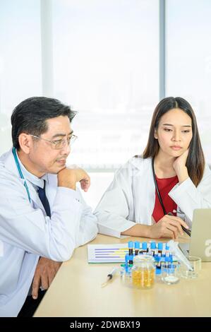 Couple of Asian adult  male doctor and Asian young female doctor wearing formal white coat teamwork brainstorm meeting with computer laptop at the hos Stock Photo