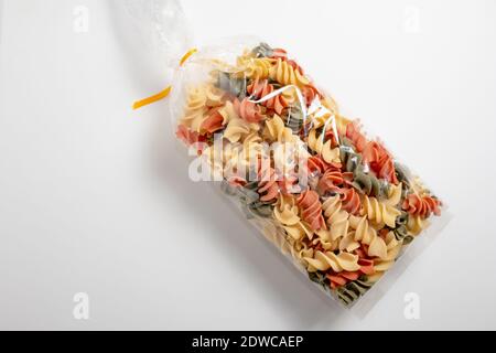 Fusilli type tricolor pasta package closed on a white surface. Concept foods rich in carbohydrates. Stock Photo