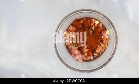 Chopped chicken fillet marinated with garlic, seasoning, paprika, and soy sauce close up in a glass bowl on marble background Stock Photo
