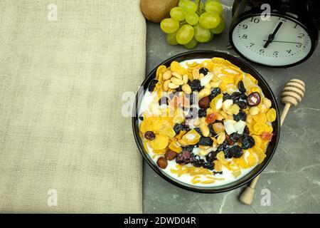 Cornflakes with milk for breakfast. Honey flakes and nuts with raisins and milk as a healthy and healthy breakfast. The clock shows six in the morning Stock Photo