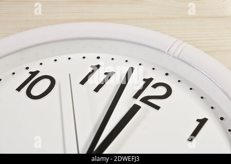 Dial of an analog clock close up on a wooden background. The time is 23:59. White dial, black numerals. Stock Photo