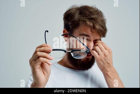 a man with narrowed eyes holds glasses in his hand on a light background vision problems Stock Photo