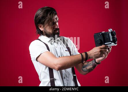 photo shooting. retro man in suspenders and bow tie. confident elegant photographer hold classical camera. journalist with vintage photo camera. formal party reporter. old fashioned bearded hipster. Stock Photo