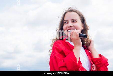 teen girl singing song in microphone on sky background, live music. Stock Photo