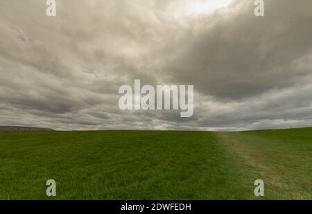 Dark stormy clouds over a green grass field. Ideal for backgrounds. Stock Photo