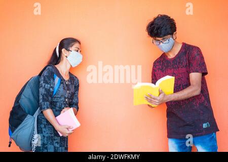 Two students in face mask discussing at college while maintaining social distance - concept of college reopen with covid-19 or coronavirus safety meas Stock Photo