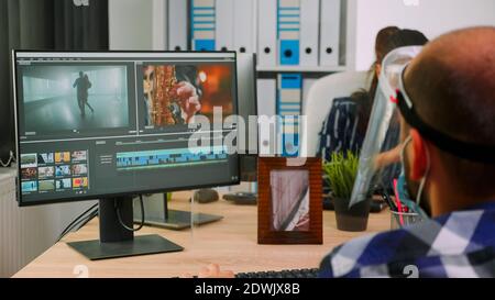 Paralysed man videographer with face mask editing video project creating content sitting in wheelchair in new normal office. Bloggers working durig global pandemic respecting social distance. Stock Photo