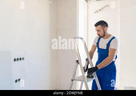 A foreman in overalls marks the wall using a laser level Stock Photo