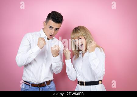 Young couple of girlfriend and boyfriend over isolated pink background very happy and excited making winner gesture with raised arms, smiling and scre Stock Photo