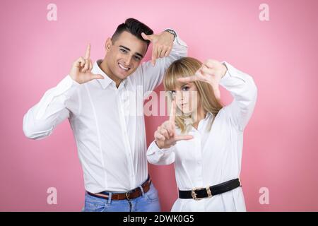Young couple of girlfriend and boyfriend over isolated pink background smiling making frame with hands and fingers with happy face Stock Photo