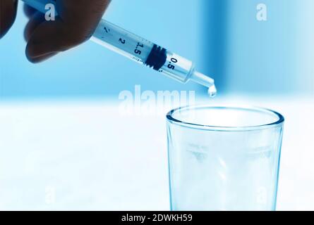 a drop falling from the spout of a test tube into a glass container in a science laboratory. Scientific experiment and medical research. Stock Photo