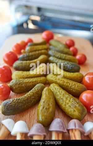Christmas tree made of pickled cucumbers, decorated with cherry tomatoes, sweet mushroom-shaped cookies below Stock Photo