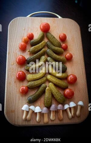 Christmas tree made of pickled cucumbers, decorated with cherry tomatoes, sweet mushroom-shaped cookies below Stock Photo