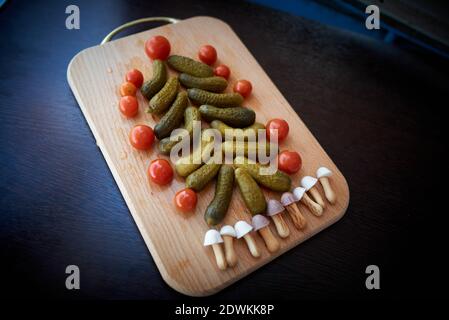 Christmas tree made of pickled cucumbers, decorated with cherry tomatoes, sweet mushroom-shaped cookies below Stock Photo