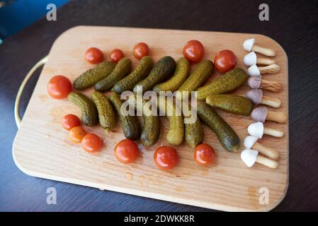 Christmas tree made of pickled cucumbers, decorated with cherry tomatoes, sweet mushroom-shaped cookies below Stock Photo