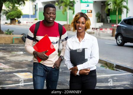 Two young students with books walking together outdoors on the road. Stock Photo