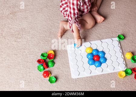 A toddler plays with a plastic mosaic on the carpet in the children's room. Early development, the Montessori method. Stock Photo