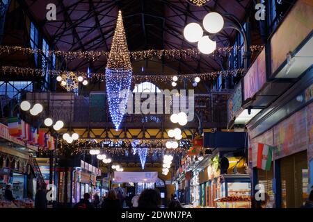 Budapest, Hungary - December 16, 2020: Christmas lights decoration on the ceiling of the large food market at Fővám square and shopping people Stock Photo