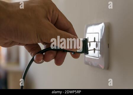 Men's hands are plugged in the power cord on the wall. Stock Photo