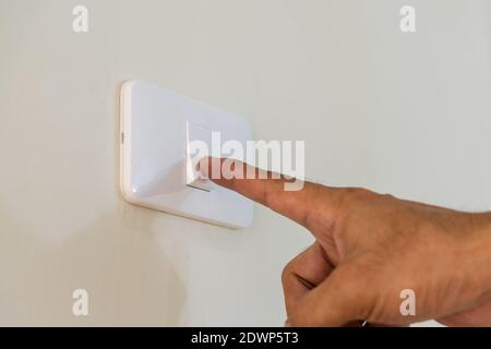 Men's fingers are extended to open the light switch on the wall. Stock Photo