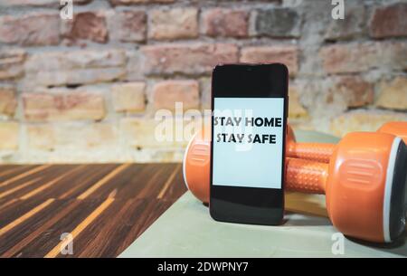 Mobile phone with text STAY HOME STAY SAFE and sports equipment isolated on a wooden floor. Stock Photo