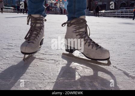 Feet in skates. Public ice-skating rink, pair of skates, scratched ice, sunny day in the winter. Girl skating on ice rink. Close-up photo. Stock Photo