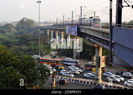 Delhi, India - October, 2016: Delhi metro train on the railway concrete bridge and traffic jam on the road below in the evening Stock Photo