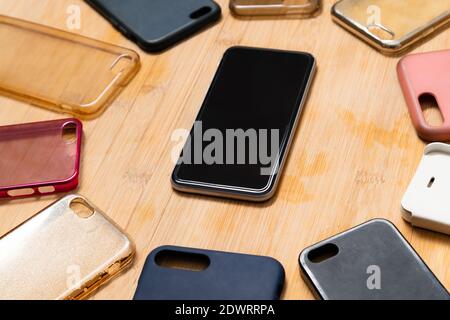 Pile of multicolored plastic back covers for mobile phones on wooden background with a phone on the side Stock Photo