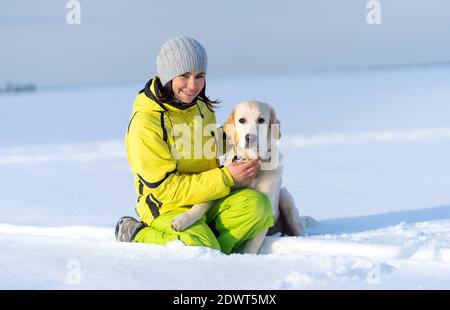 Happy woman caressing cute young retriever dog sitting in snow Stock Photo