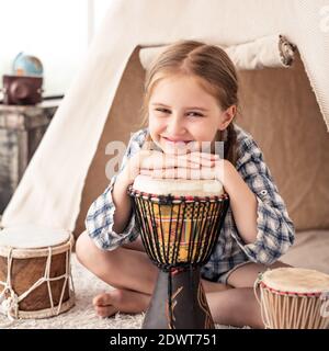 Portrait of Little girl playing on traditional african djembe drums sitting in wigwam in kids room Stock Photo