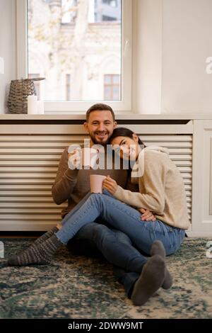 Romantic couple at home. An Attractive young woman and handsome man are enjoying spending time together while siting coddling with cups of tea in hand Stock Photo