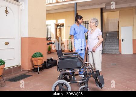 Happy Senior woman with  walking stick in  Wheelchair with her caregiver at home . They are talking and laughing together. Stock Photo