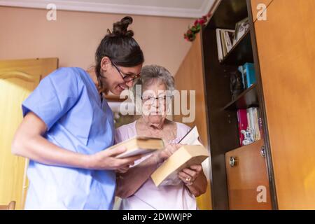 Happy Senior woman with her caregiver at home reading a book. Senior home care concept. Stock Photo