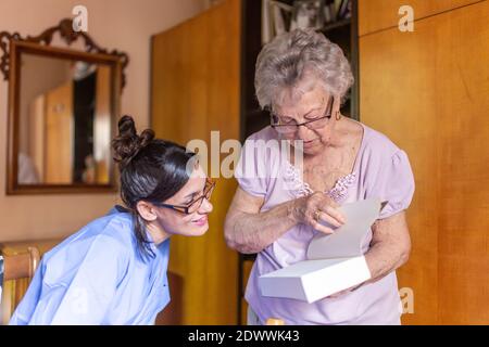 Happy Senior woman with her caregiver at home reading a book. Senior home care concept. Stock Photo