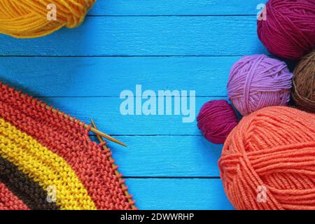 Hobby and knitting concepts.  Multi-colored clews  and balls of wool on blue rustic table. Unfinished striped knitwork with knitting needles. Copy spa Stock Photo