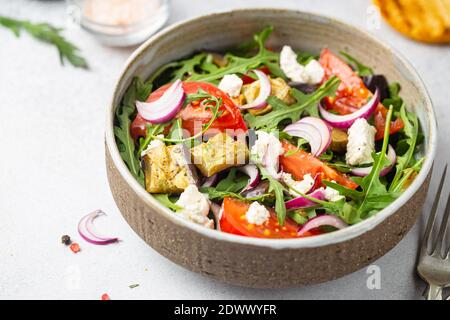 Eggplant salad with tomatoes, arugula and feta cheese in a bowl on white background Stock Photo