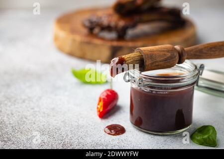 Barbecue sauce in glass jar with basting brush over gray stone table with copy space. Stock Photo