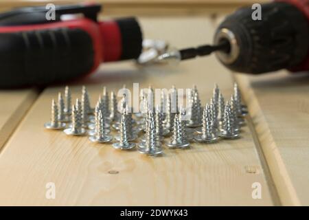 Electric drill with drill bits, screws on wooden background. Bunch of screws on wood planks. Assorted tools. Handyman professional DIY project workpla Stock Photo