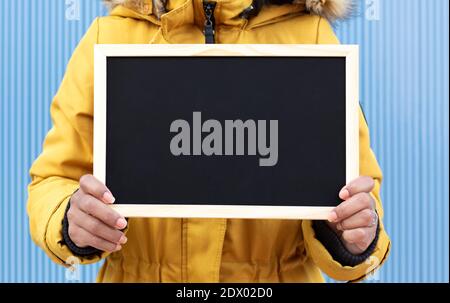 Close up of unrecognizable person holding a blank chalkboard. Blue background. Space for text. Stock Photo
