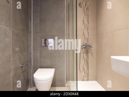 Front view of small size bathroom in modern style. Toilet interior tiled of beige mosaic and big scale tiles with gray marble stone texture Stock Photo