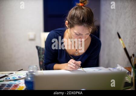 Portrait of creative young woman seated at table in an artists' workshop, working on painting Stock Photo