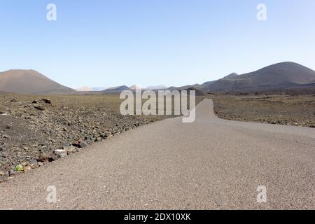 Empty road at volcanic landscape in Lanzarote's Timanfaya National Park. Nobody on sight on sunny day at tourist attraction landmark in Canary Islands Stock Photo